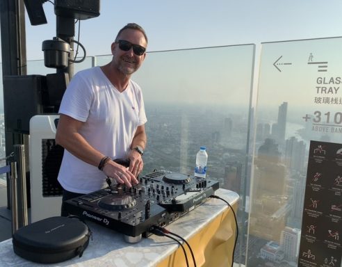 DJ bei Sonnenuntergang auf einer Dachterrasse mit Blick auf die Stadt.
