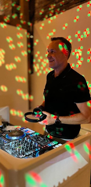DJ Flemming DJ steht an einem Mixer, umgeben von farbigen Lichtpunkten auf einer Wand.